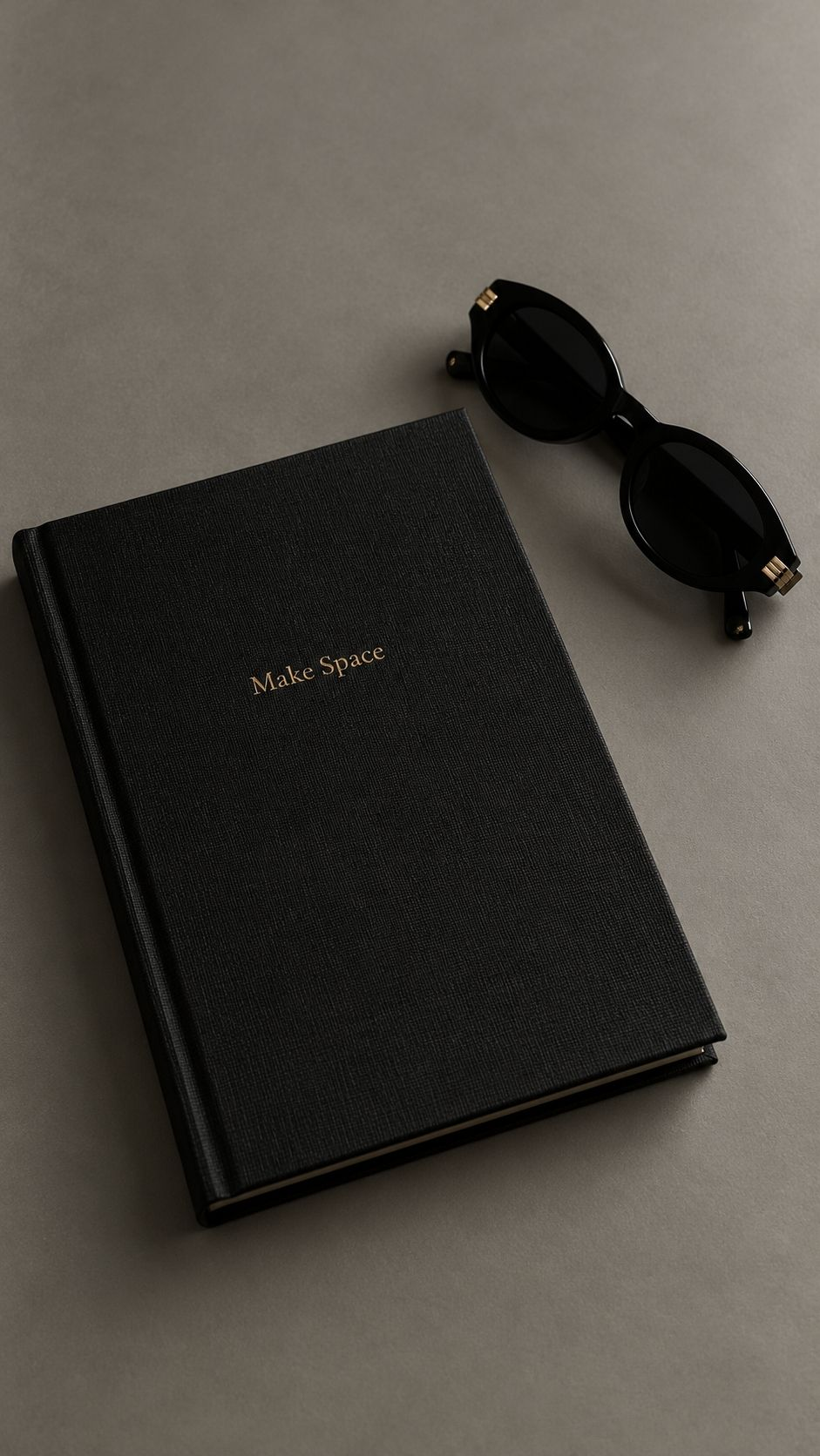 A black linen journal and black sunglasses on a stone surface
