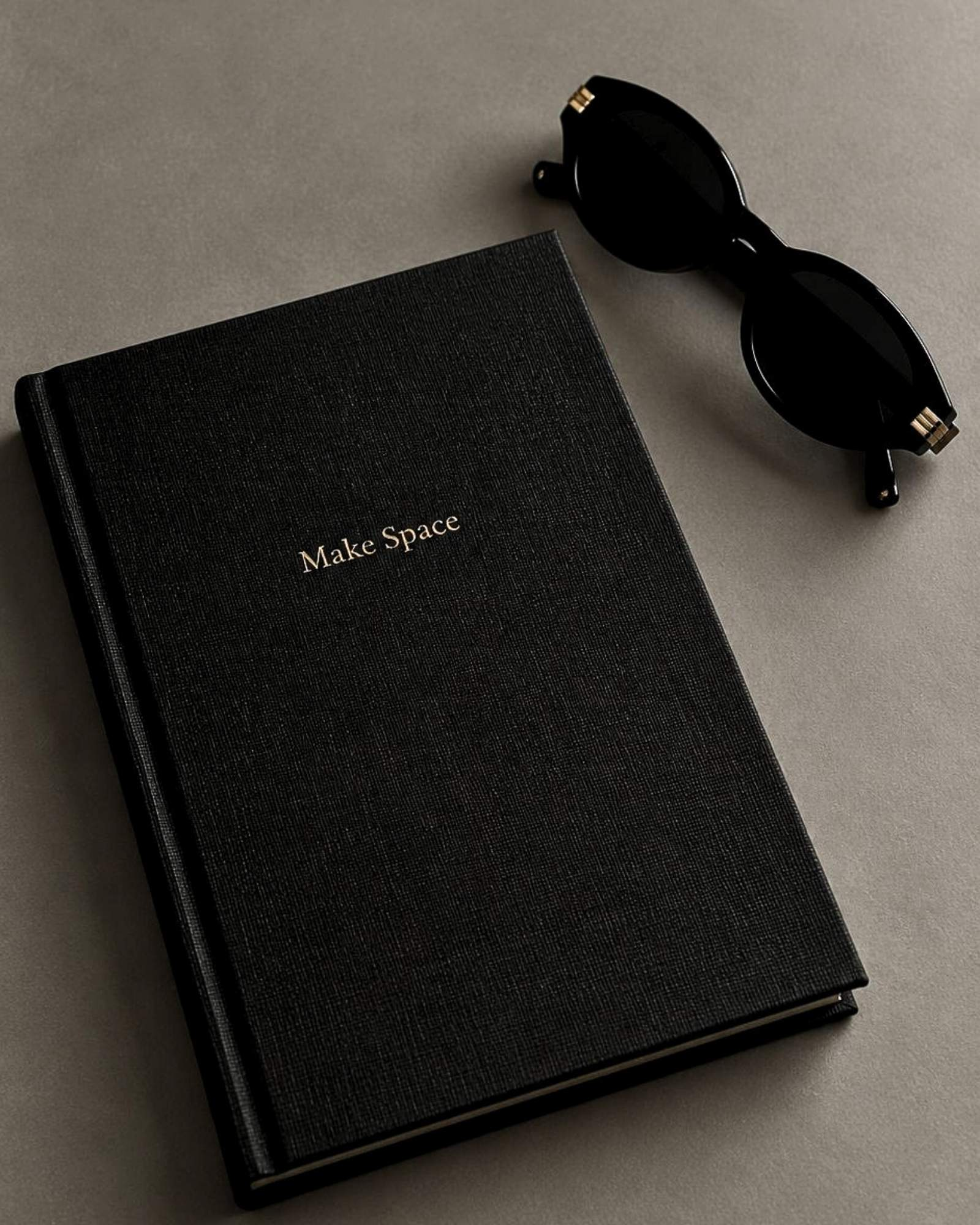 A black linen journal and black sunglasses on a stone surface